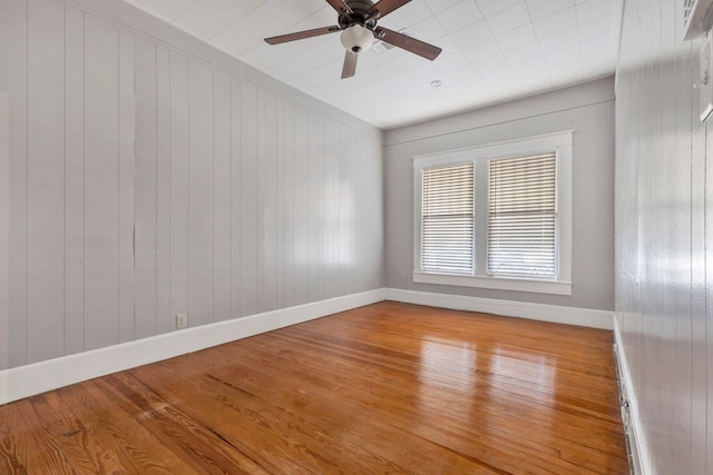 spare room with ceiling fan, wood-type flooring, and wood walls