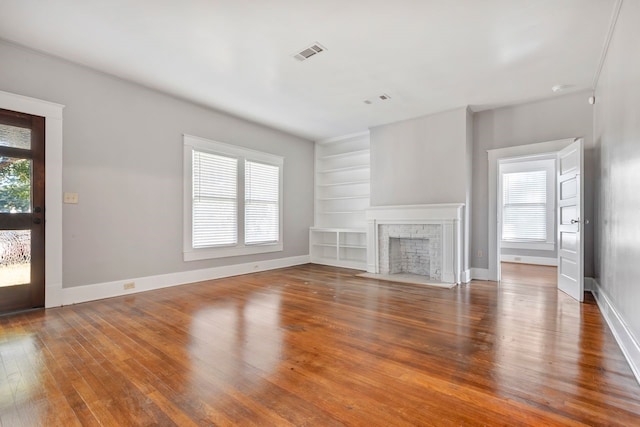 unfurnished living room featuring built in shelves, plenty of natural light, and wood-type flooring