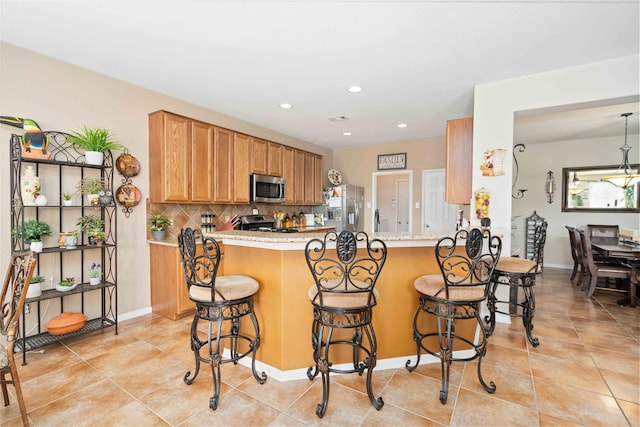 kitchen with kitchen peninsula, a breakfast bar area, stainless steel appliances, tasteful backsplash, and light tile patterned flooring