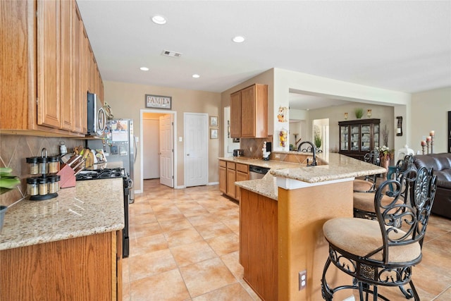 kitchen featuring appliances with stainless steel finishes, tasteful backsplash, kitchen peninsula, light stone counters, and a breakfast bar area