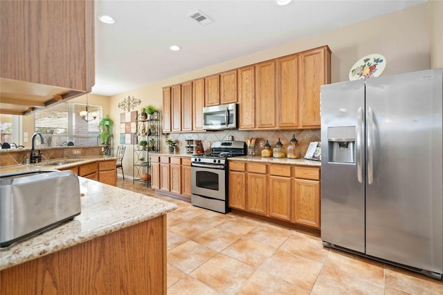 kitchen with appliances with stainless steel finishes, decorative backsplash, decorative light fixtures, light stone countertops, and sink