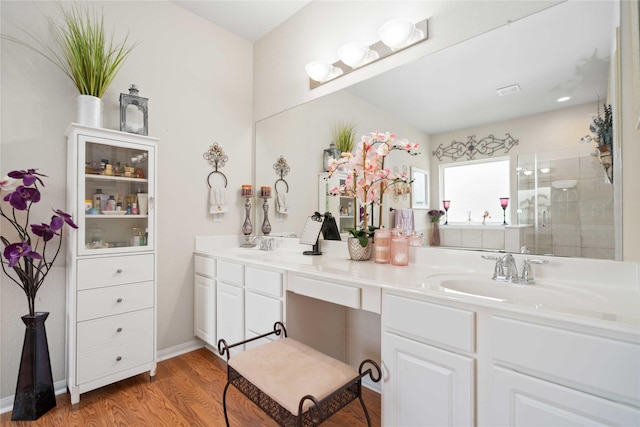 full bath featuring wood finished floors, a sink, baseboards, a shower stall, and double vanity