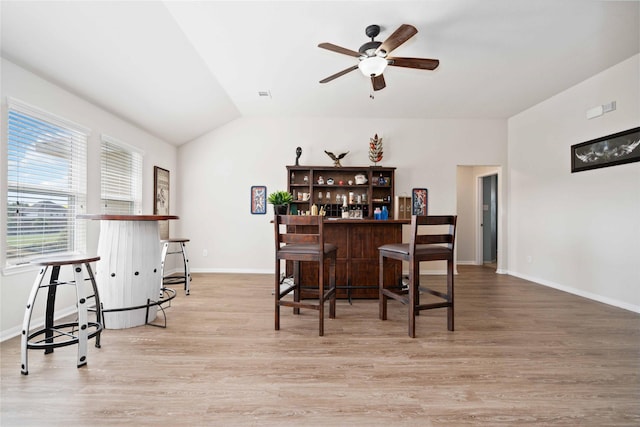 bar featuring baseboards, a ceiling fan, light wood-style flooring, vaulted ceiling, and a bar