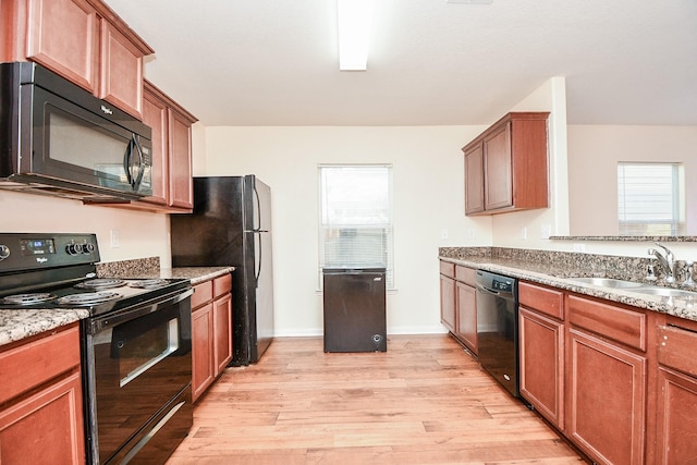 kitchen featuring black appliances, light hardwood / wood-style floors, light stone countertops, and sink