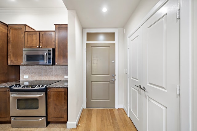 kitchen featuring tasteful backsplash, ornamental molding, stainless steel appliances, light hardwood / wood-style flooring, and dark stone countertops