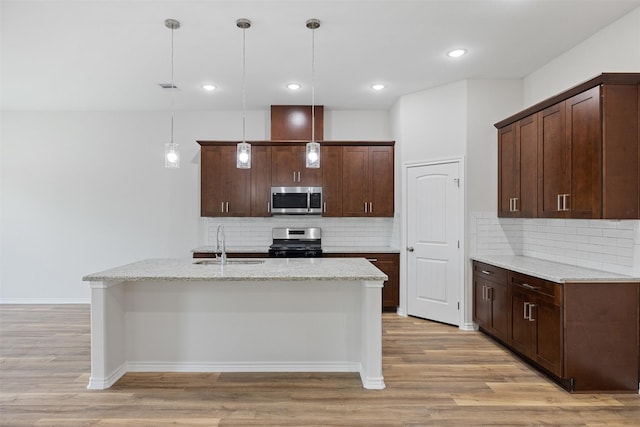 kitchen featuring sink, decorative light fixtures, light wood-type flooring, dark brown cabinets, and stainless steel appliances