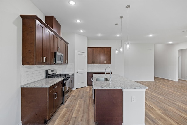 kitchen with sink, decorative light fixtures, a center island with sink, appliances with stainless steel finishes, and light wood-type flooring