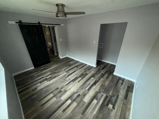 unfurnished room featuring a barn door, ceiling fan, and dark hardwood / wood-style floors