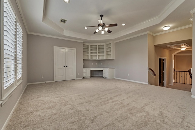 unfurnished living room with carpet floors, built in desk, crown molding, and a tray ceiling