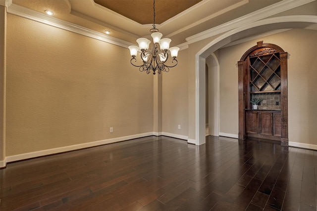 unfurnished room featuring ornamental molding, a raised ceiling, dark wood-type flooring, and a notable chandelier