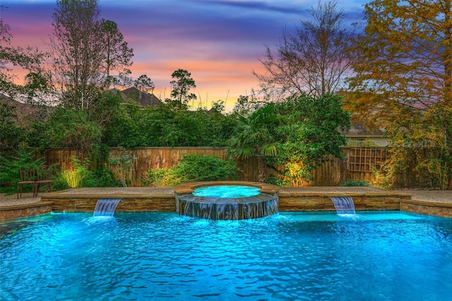 pool at dusk featuring pool water feature and an in ground hot tub