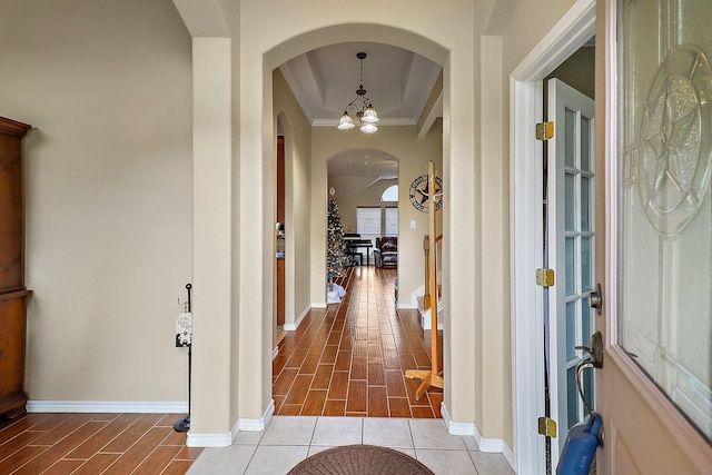 hall featuring a tray ceiling, ornamental molding, a chandelier, and light wood-type flooring