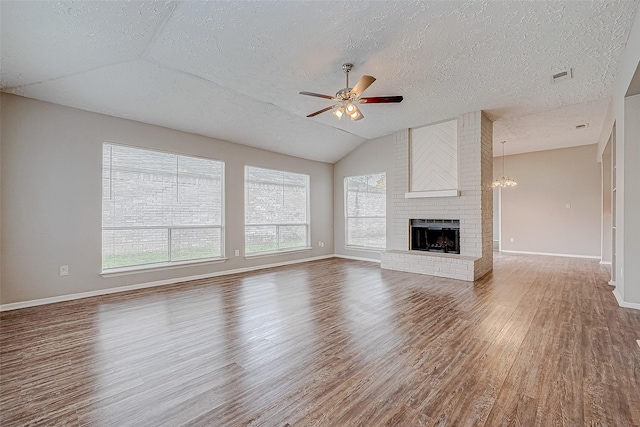 unfurnished living room with a textured ceiling, ceiling fan with notable chandelier, a fireplace, hardwood / wood-style floors, and lofted ceiling