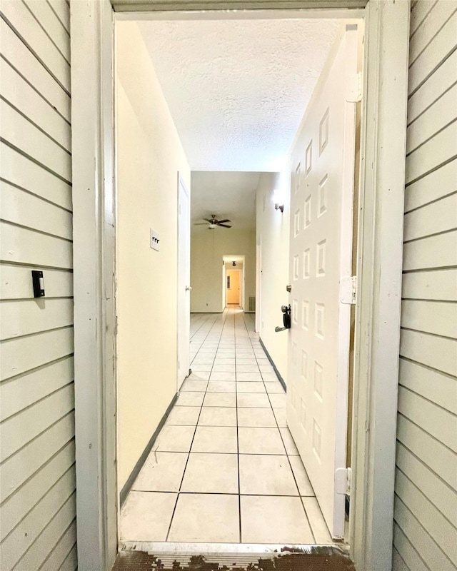 hallway featuring wooden walls, light tile patterned floors, and a textured ceiling