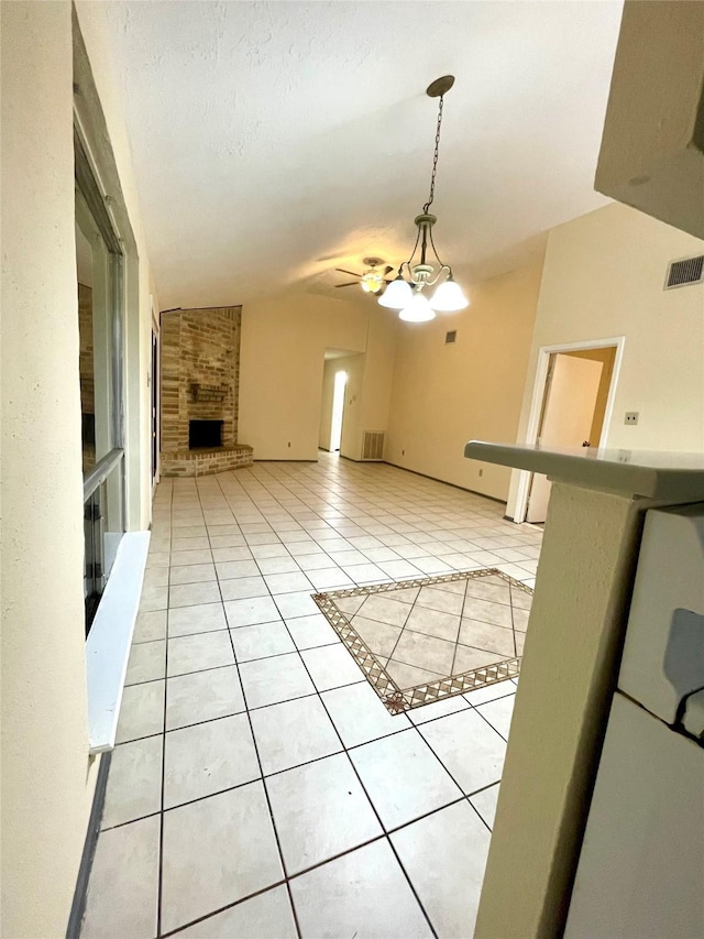 unfurnished living room with ceiling fan with notable chandelier, light tile patterned floors, a fireplace, and vaulted ceiling