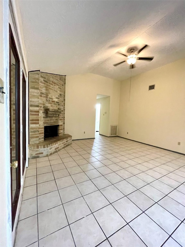 unfurnished living room with ceiling fan, a fireplace, light tile patterned flooring, and a textured ceiling