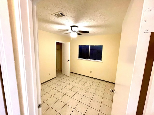 unfurnished room featuring ceiling fan, light tile patterned flooring, and a textured ceiling