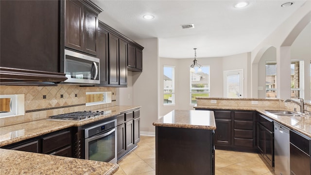 kitchen with sink, stainless steel appliances, pendant lighting, dark brown cabinets, and a kitchen island