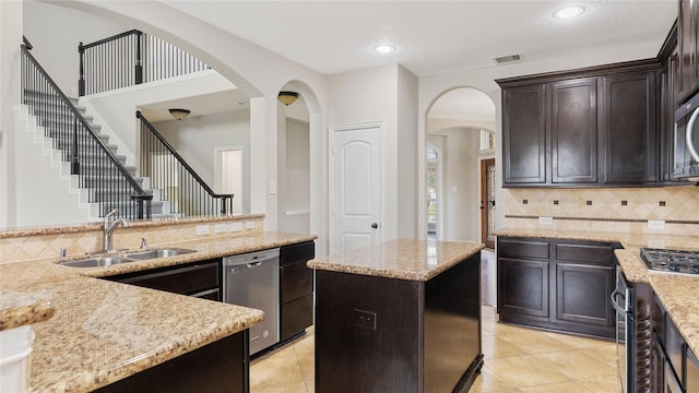 kitchen featuring a center island, sink, decorative backsplash, light stone countertops, and appliances with stainless steel finishes