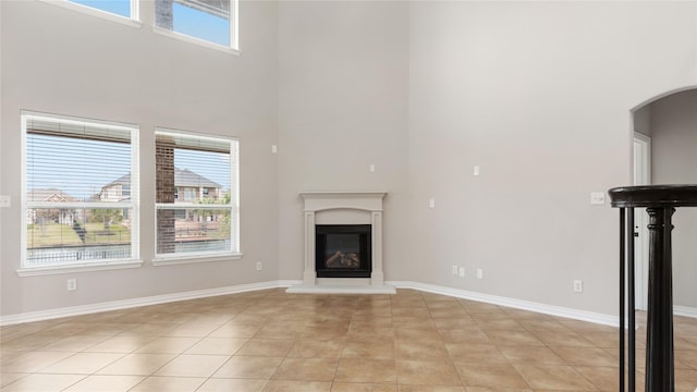 unfurnished living room with plenty of natural light, light tile patterned floors, and a high ceiling