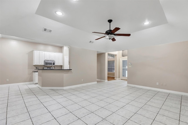 unfurnished living room featuring a raised ceiling, ceiling fan, and light tile patterned flooring