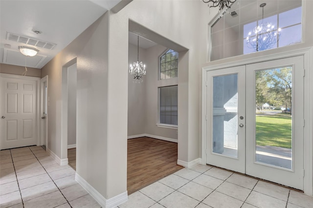 foyer featuring a chandelier, french doors, light wood-type flooring, and a towering ceiling