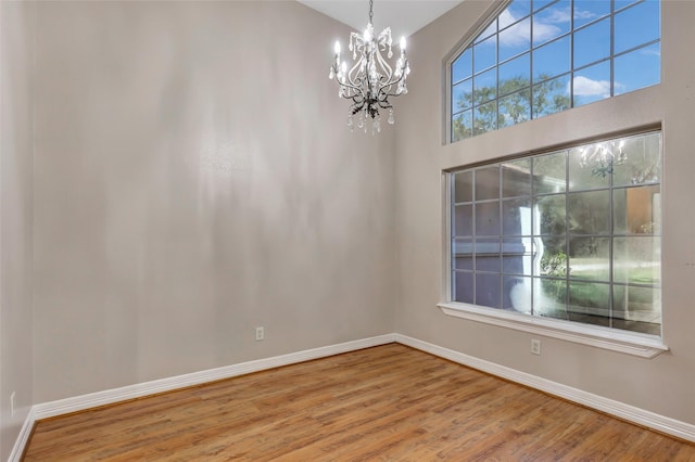 spare room with a towering ceiling, a chandelier, and hardwood / wood-style flooring