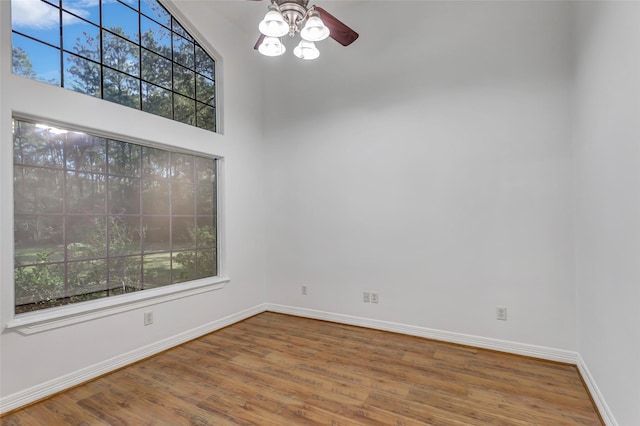 unfurnished room featuring ceiling fan, a towering ceiling, and wood-type flooring