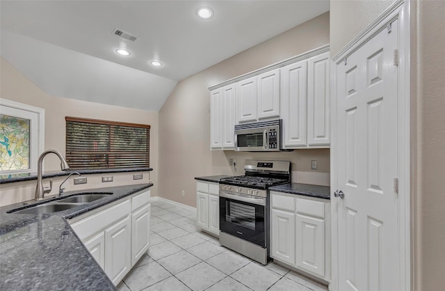 kitchen with lofted ceiling, white cabinets, sink, light tile patterned floors, and appliances with stainless steel finishes