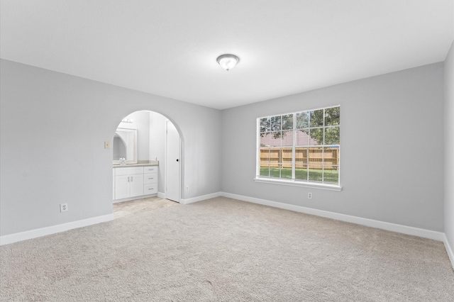 unfurnished bedroom with light carpet, baseboards, arched walkways, and ensuite bathroom