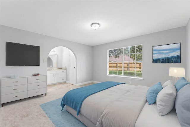 bedroom featuring arched walkways, light carpet, a sink, ensuite bath, and baseboards