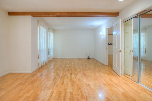 empty room with beam ceiling and light hardwood / wood-style floors