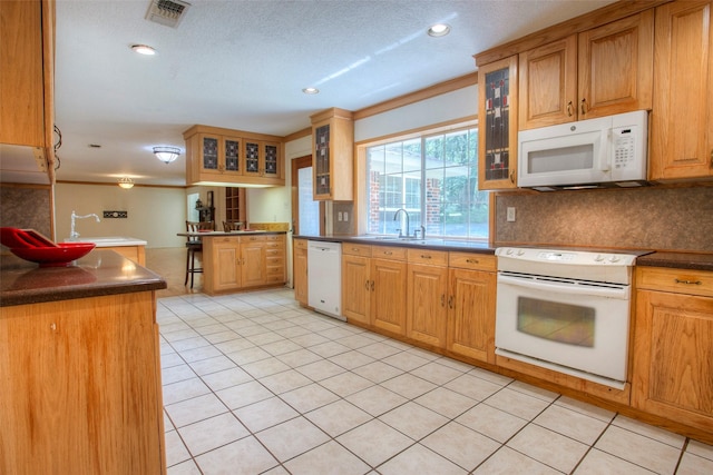 kitchen with glass insert cabinets, dark countertops, white appliances, and visible vents