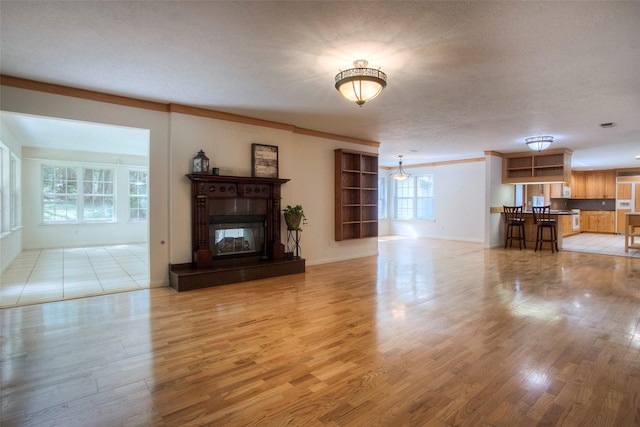 unfurnished living room featuring light wood-style floors, crown molding, a textured ceiling, and a glass covered fireplace