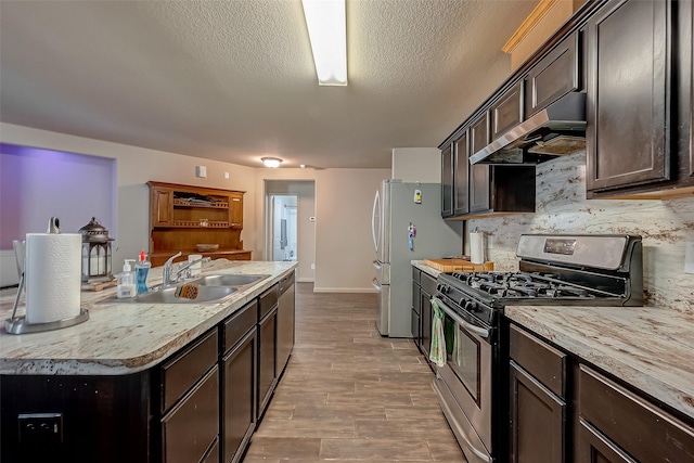 kitchen with appliances with stainless steel finishes, dark brown cabinets, a textured ceiling, sink, and exhaust hood