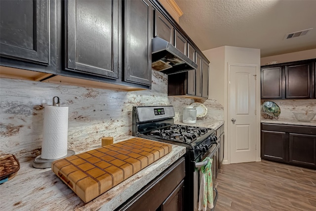 kitchen featuring stainless steel gas range, tasteful backsplash, a textured ceiling, dark brown cabinets, and light wood-type flooring