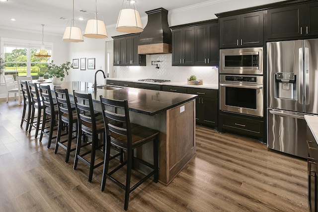 kitchen with a kitchen island with sink, sink, custom range hood, and appliances with stainless steel finishes