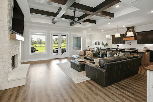 living room with coffered ceiling, a stone fireplace, ceiling fan, beamed ceiling, and wood-type flooring