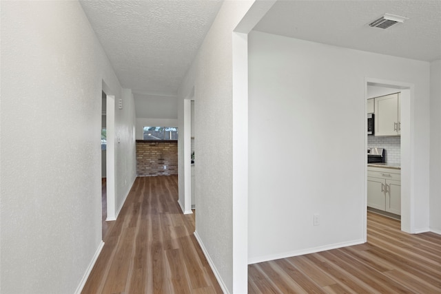 hall with light hardwood / wood-style floors and a textured ceiling