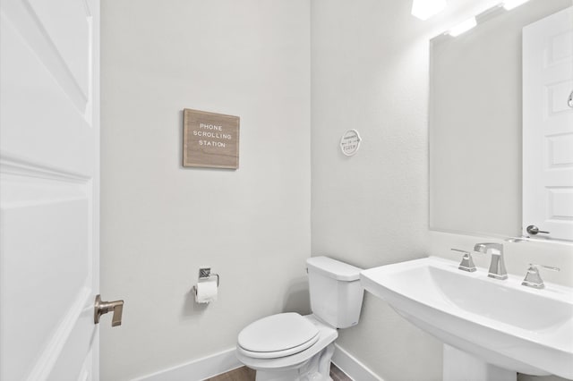 half bath with baseboards, a sink, toilet, and wood finished floors