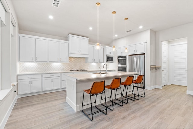 kitchen featuring stainless steel appliances, a sink, white cabinetry, decorative backsplash, and light wood finished floors