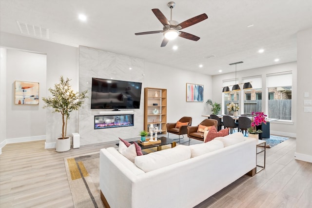 living room featuring light wood finished floors, baseboards, a fireplace, and visible vents