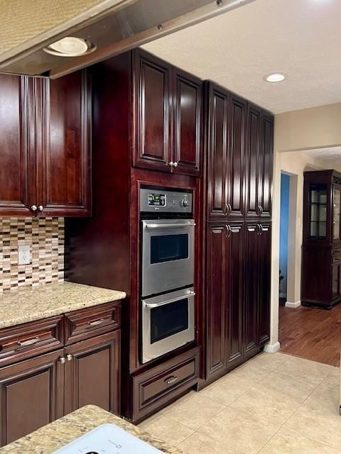 kitchen featuring light stone countertops, stainless steel double oven, tasteful backsplash, and light tile patterned flooring