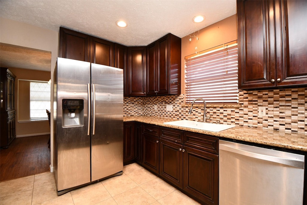 kitchen with tasteful backsplash, sink, light tile patterned floors, light stone counters, and stainless steel appliances