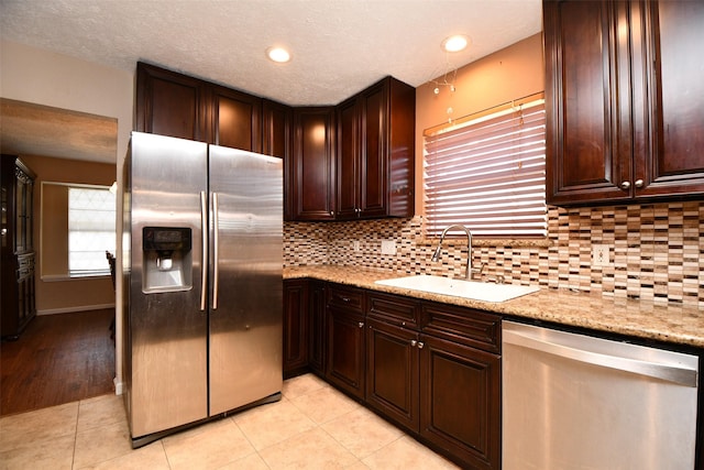 kitchen with tasteful backsplash, sink, light tile patterned floors, light stone counters, and stainless steel appliances