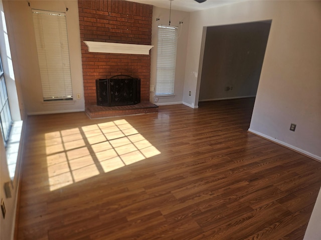 unfurnished living room featuring a brick fireplace, ceiling fan, and dark wood-type flooring