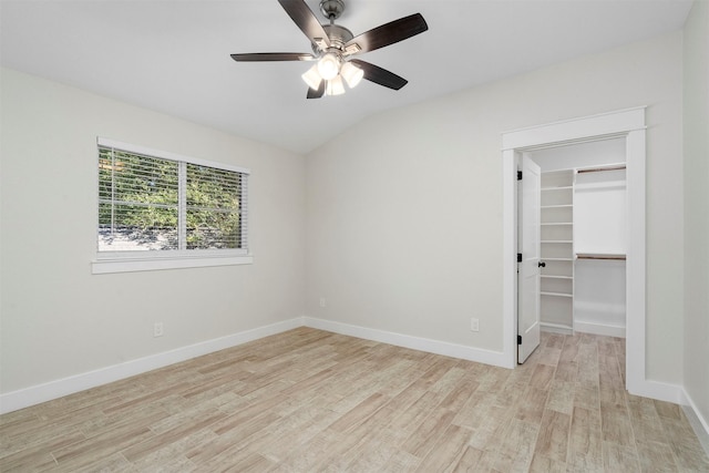 unfurnished bedroom with lofted ceiling, ceiling fan, light wood-type flooring, a spacious closet, and a closet