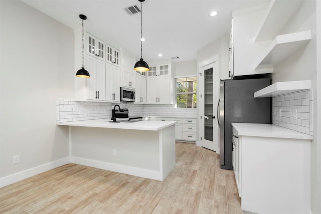 kitchen featuring kitchen peninsula, stainless steel appliances, light hardwood / wood-style floors, white cabinetry, and hanging light fixtures