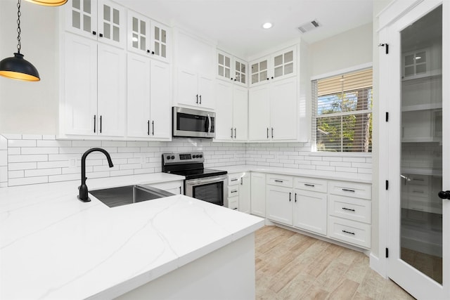 kitchen with white cabinets, sink, hanging light fixtures, light stone countertops, and appliances with stainless steel finishes