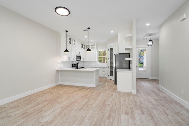 kitchen with white cabinetry, stainless steel appliances, kitchen peninsula, pendant lighting, and light wood-type flooring